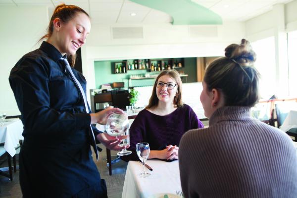 A Student of the Hospitality Management Diploma program serving two women